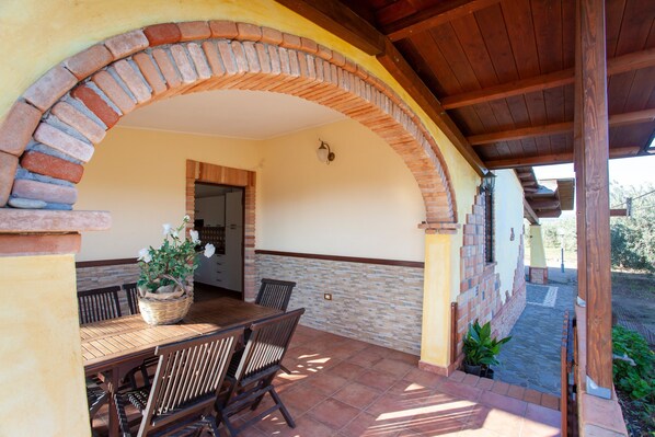 Un patio techado con un arco de ladrillo, una mesa de madera con sillas y una planta en maceta.