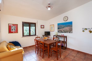 A dining area with a wooden table and chairs, a television, and artwork on the walls. - Pet-friendly Holiday Apartment "A contatto con la natura - Orosei" with Garden, Terrace & Wi-Fi (Orosei)