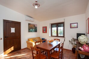 Un comedor con una mesa de madera, sillas, un sofá, una ventana con persianas y un florero con plantas.