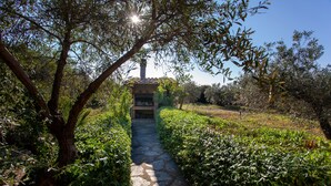 A stone pathway leading to a building with a chimney, surrounded by lush greenery and trees.