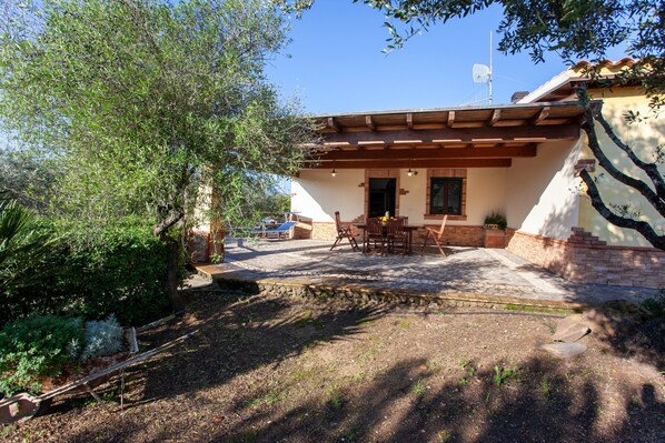 Un patio con mobiliario exterior, un sendero de piedra y un edificio con tejado de tejas y paredes de ladrillo.