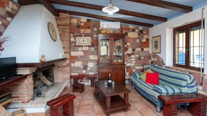 A living room with a fireplace, stone wall, wooden furniture, and a television.