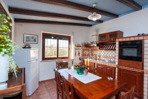 A kitchen with wooden cabinets, a refrigerator, a dining table with chairs, and a window with a view.