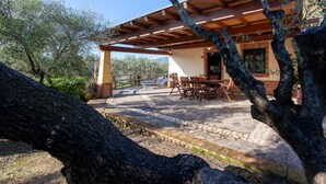 An outdoor patio with stone flooring, wooden furniture, and a pergola structure.