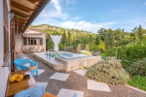 Une terrasse dotée d’un jacuzzi, de mobilier d’extérieur et offrant une vue sur la végétation environnante.