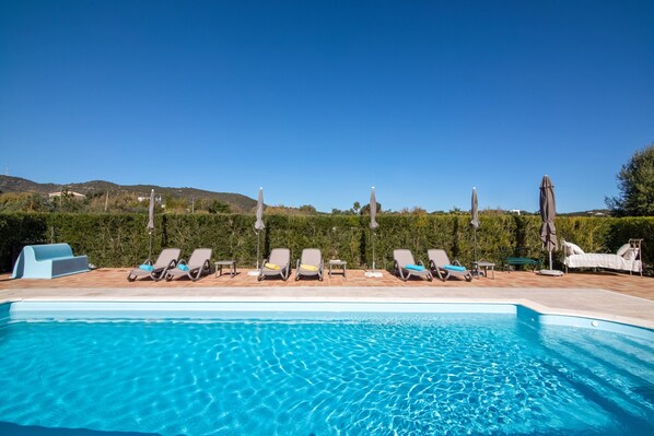 A clear blue pool with lounge chairs and umbrellas, surrounded by greenery and hills. - Villa 'Oliva AL' with Nature Views, Pool, Garden, Terrace, Wi-Fi & AC (Moncarapacho)