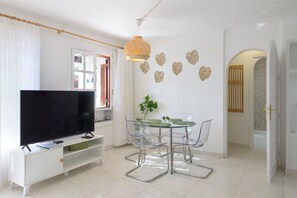 A modern living room with a flat-screen TV, a glass dining table with chairs, and a decorative wall piece. - Holiday Apartment Puerto Chico C by Beach with Shared Pool & Wi-Fi (Playa Blanca)