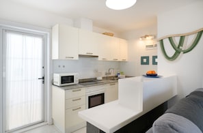 Une cuisine compacte avec des meubles blancs, un four à micro-ondes, un évier et un petit four.