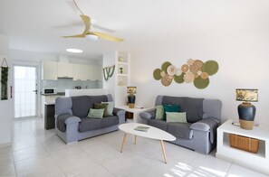 A modern living room with two grey sofas, a white coffee table, and a ceiling fan. - Holiday Apartment Puerto Chico C by Beach with Shared Pool & Wi-Fi (Playa Blanca)