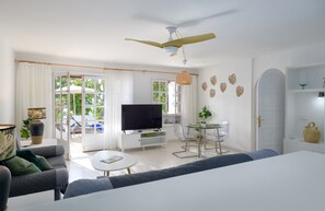 A modern living room with a flat-screen TV, a ceiling fan, and a dining area with a glass table and chairs.