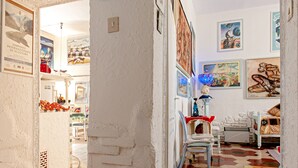 Ein Zimmer mit weißer Wand, Fliesenboden, einem Bett, einem Sessel und einem Tisch mit Lampe.