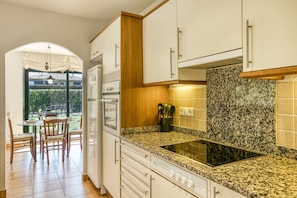 A kitchen with granite countertops, white cabinets, a built-in oven, and a dining area with a table and chairs.