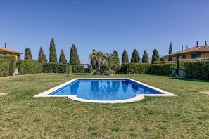 Une piscine rectangulaire dont les bords sont recouverts de carreaux, entourée d’une pelouse bien entretenue et de haies.