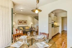 A dining area with a glass table, chairs, and a kitchen in the background.