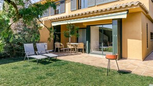 A two-story building with a patio area featuring outdoor furniture and a small table. - Family villa in Torremirona Resort (Navata)