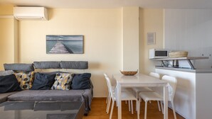 A living room with a sofa, a dining table with chairs, a kitchen area with a microwave, and a painting on the wall. - Apartment with Sea View, Balcony, and Air Conditioning (Almunecar)
