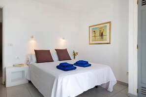 A neatly made bed with white and brown bedding, a bedside table with a book, and a framed picture on the wall.