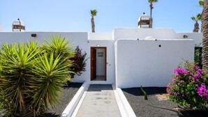 Un bâtiment aux murs blancs, avec une porte, des palmiers et un ciel dégagé.