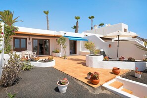 A white building with a patio area, outdoor seating, and potted plants.