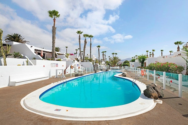 A swimming pool with a clear blue water, surrounded by white walls and palm trees.