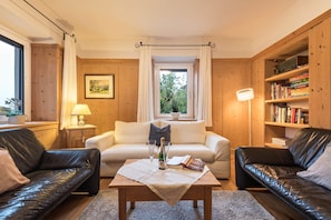 A cozy living room with a sofa, a coffee table, a bookshelf, and a window with curtains. - Holiday Apartment 'Rosa Seis' with Mountain View, Wi-Fi & Garden (Seis)