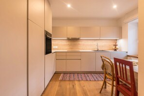 A modern kitchen with wooden cabinets, a built-in oven, and a small dining area with a chair and table. - Holiday Apartment 'Rosa Seis' with Mountain View, Wi-Fi & Garden (Seis)