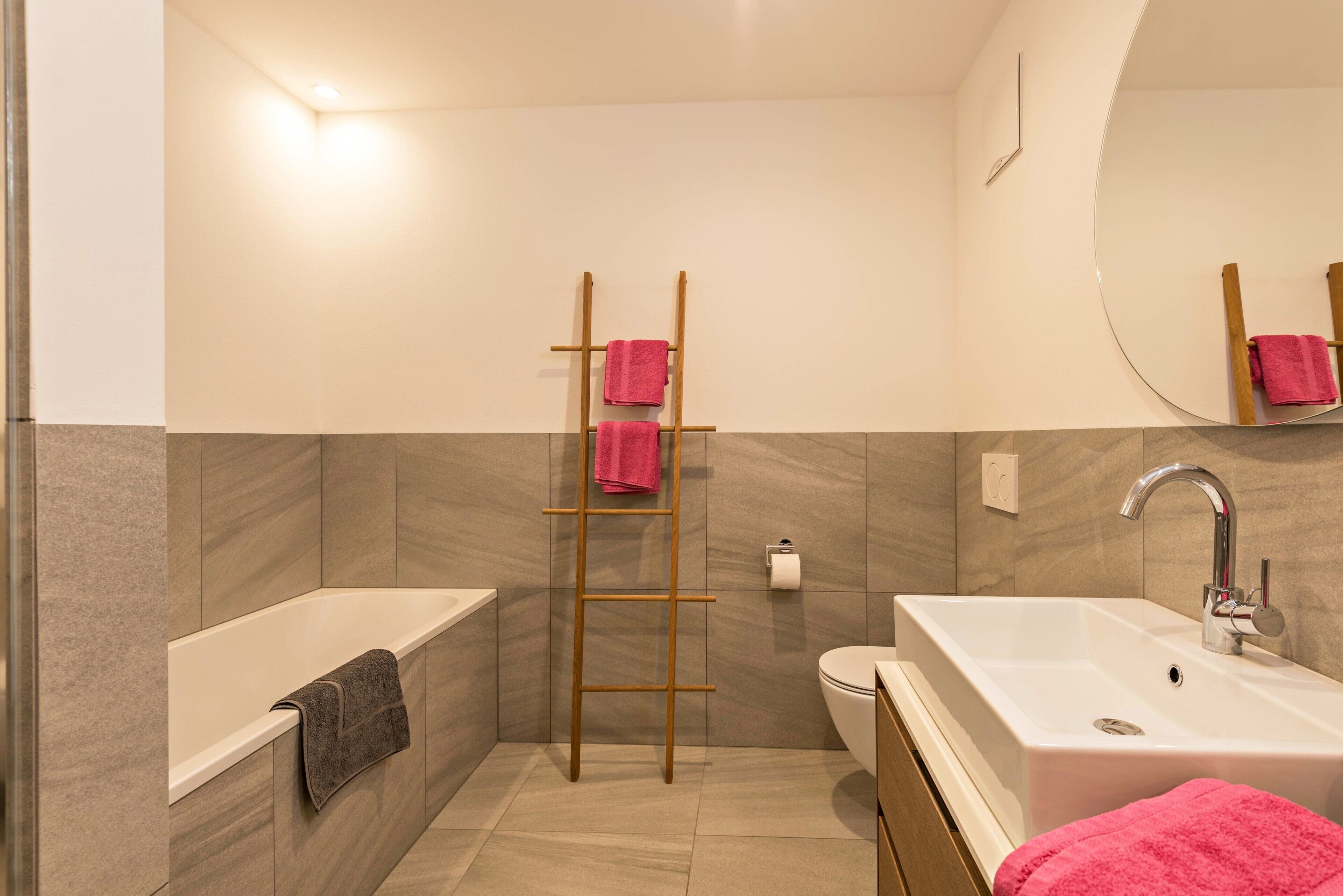 A bathroom with a bathtub, a sink, a toilet, a wooden ladder, and a mirror.