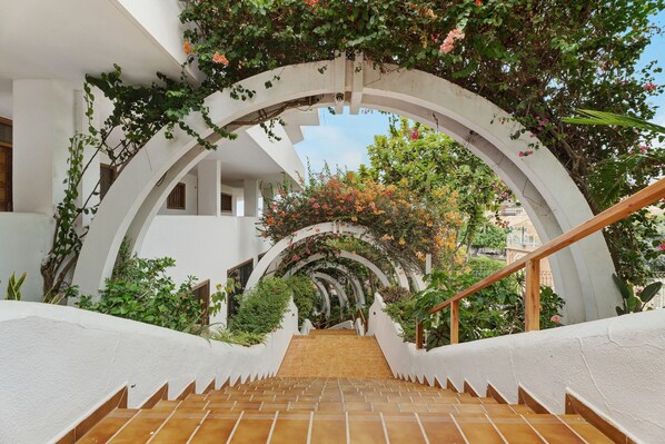 A staircase with white walls and a wooden handrail, leading to an outdoor area with greenery and a view of buildings.