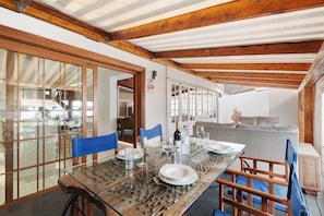 A dining area with a glass table, blue chairs, and a sofa in the background.