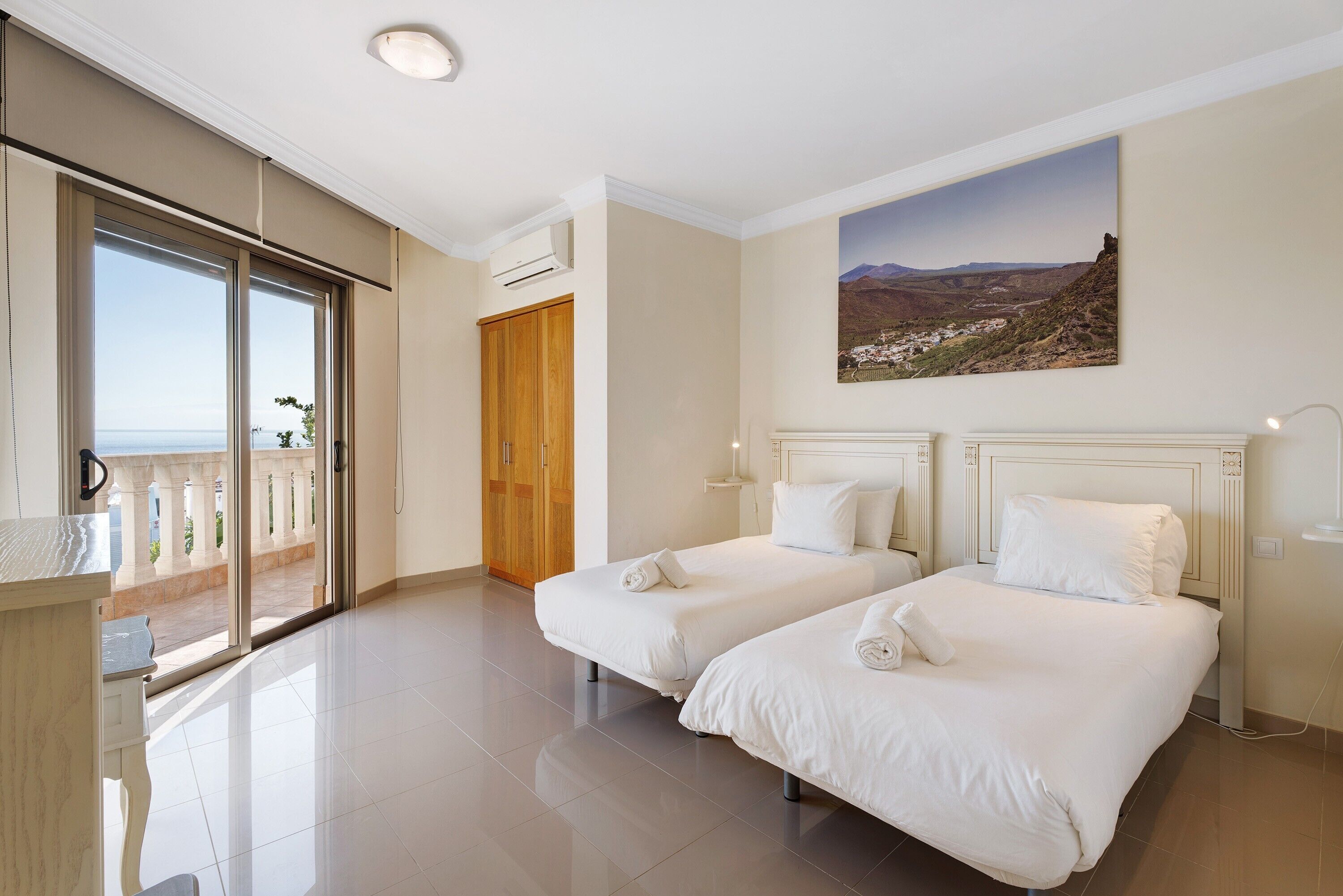 A hotel room with two beds, a balcony, and a painting of a landscape.