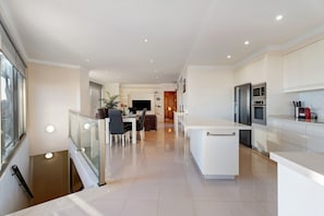A modern kitchen with white cabinetry, a dining area with a table and chairs, and a staircase leading to an upper floor.