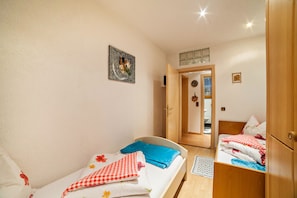 A bedroom with two single beds, a wooden wardrobe, a small bathroom, and a hallway leading to another room.