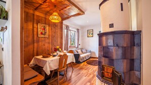A cozy room with a wooden dining table, a sofa, a fireplace, and a window with curtains. - Hoferhof Apartement 'Bergzauber' with Mountain View, Garden & Wi-Fi (Schenna)