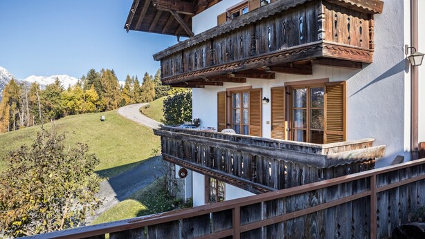 A traditional chalet with a wooden balcony, a winding road, and a mountainous backdrop. - Hoferhof Apartement 'Bergzauber' with Mountain View, Garden & Wi-Fi (Schenna)