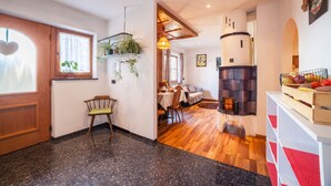 A room with a wooden door, a window with a heart-shaped decoration, a dining area with a table and chairs, a fireplace, and a shelf with plants. - Hoferhof Apartement 'Bergzauber' with Mountain View, Garden & Wi-Fi (Schenna)
