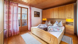 Un dormitorio con paneles de madera, una cama, lámparas de noche, una ventana con cortinas y un cuadro en la pared.