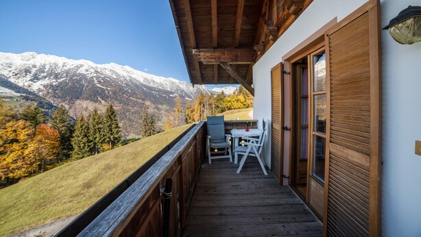 Un balcón de madera con una mesa y sillas, con vistas a un paisaje montañoso.