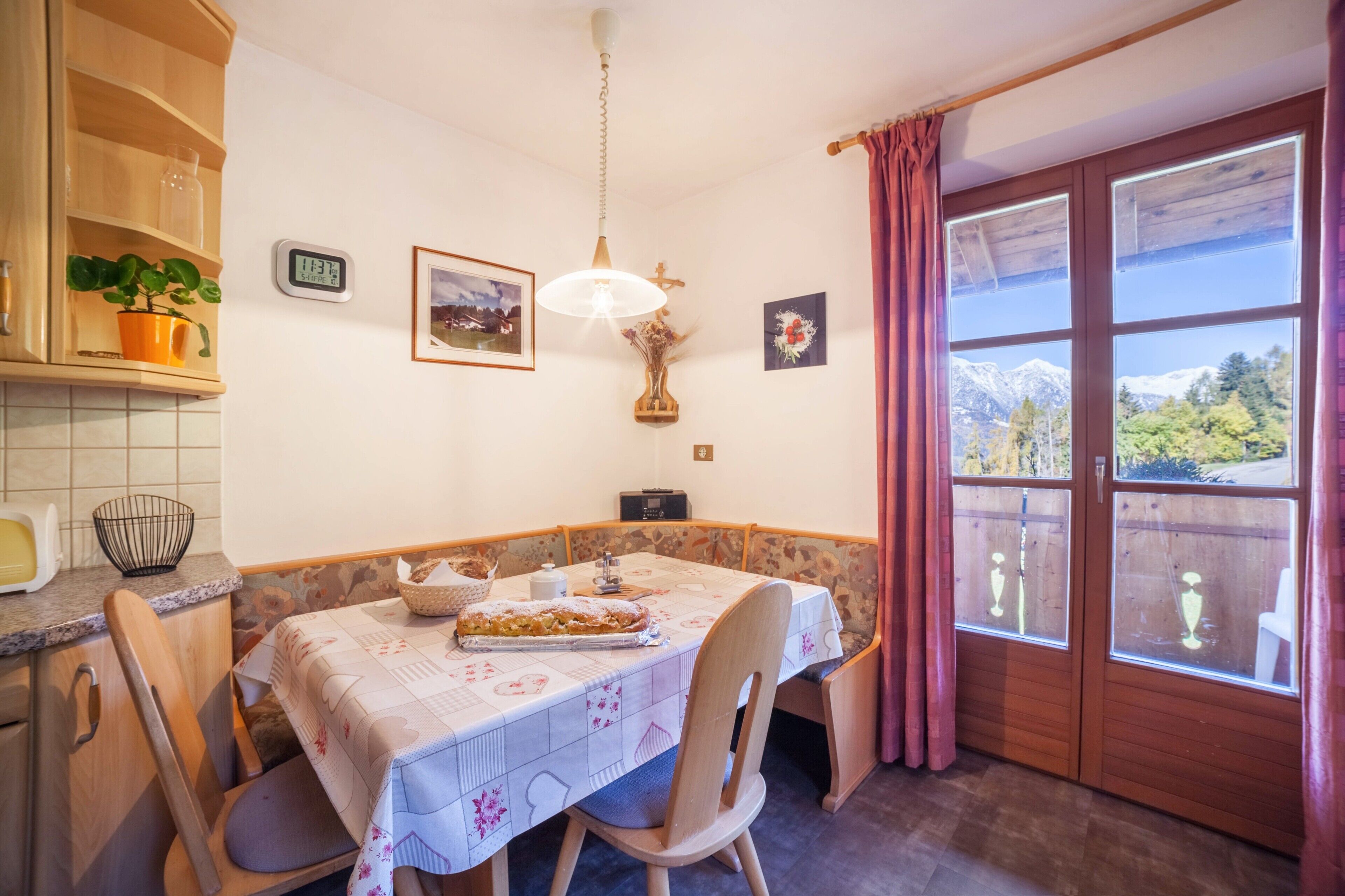 Un coin repas avec une table dressée pour deux personnes, une horloge et une fenêtre donnant sur les montagnes.