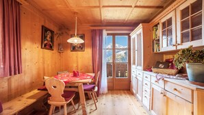 Un interior de madera con una mesa de comedor, sillas, un banco, una zona de cocina con armarios, una ventana con vistas a montañas y una lámpara colgante.