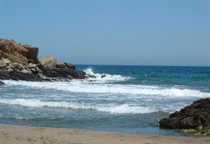 A coastal beach with waves, rocky cliffs, and clear blue sky.