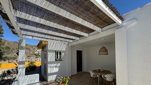 Eine überdachte Terrasse mit Tisch, Stühlen, einem Korpusfußhocker und Topfpflanzen.
