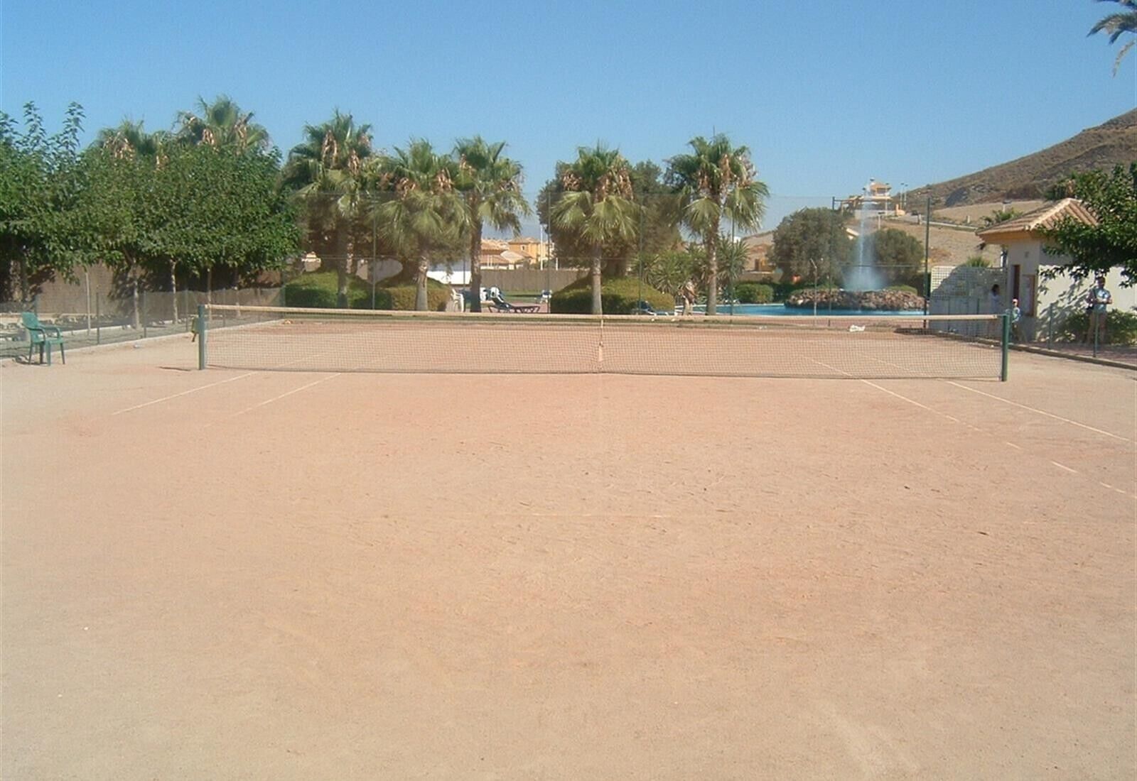 An outdoor tennis court with a net, surrounded by trees and a clear sky.