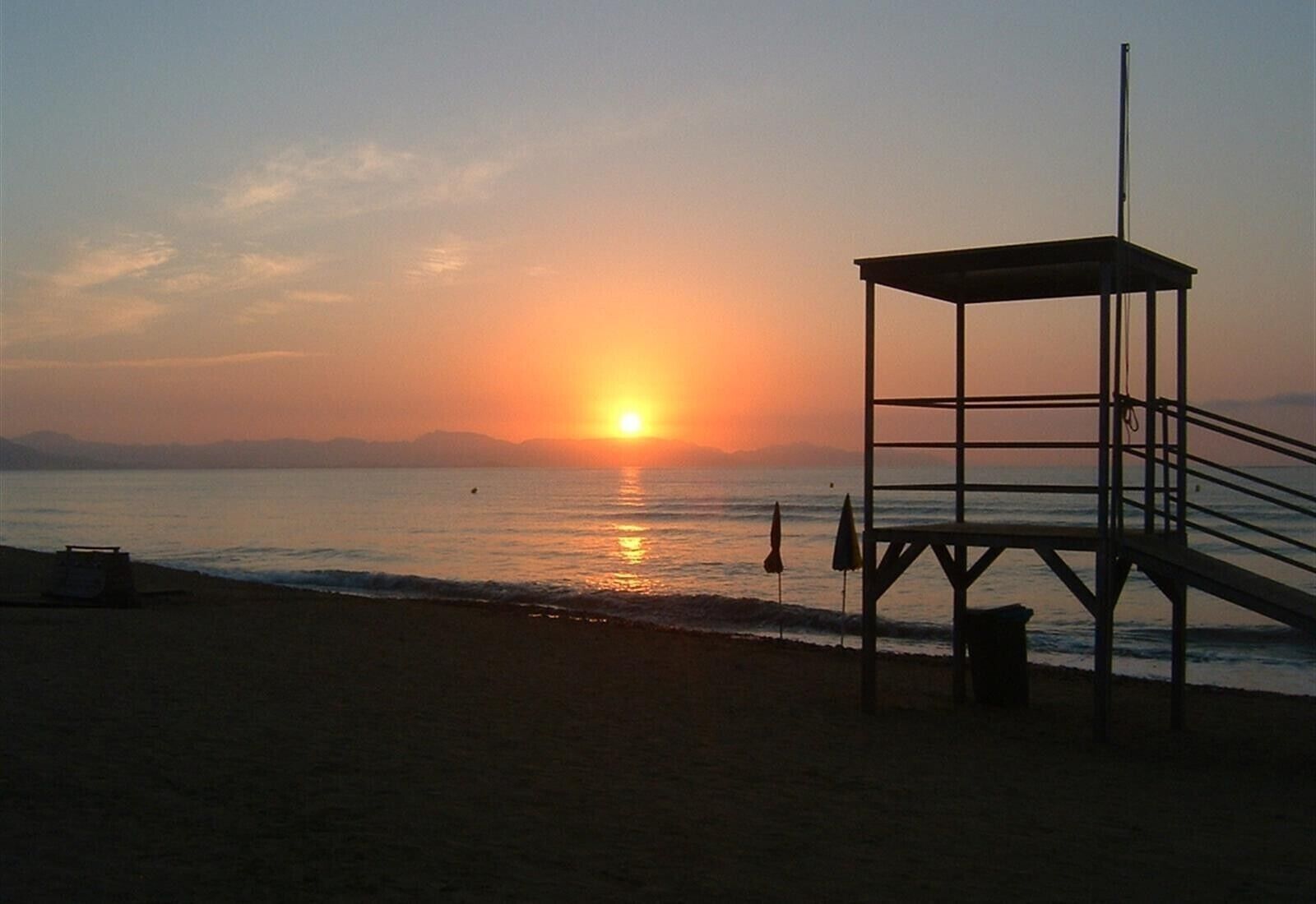 Una playa con una torre de salvavidas, agua tranquila y un atardecer.