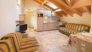 A cozy loft-style room with a kitchenette, a television, and two striped sofas. - 'Appartamento 8' with Mountain View, Shared Garden & Wi-Fi (Livigno)