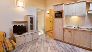 A compact kitchen with wooden cabinets, a built-in oven, a television, and a small seating area. - 'Appartamento 8' with Mountain View, Shared Garden & Wi-Fi (Livigno)