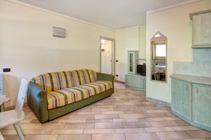 A room with a sofa, a dining table, and kitchen cabinets.