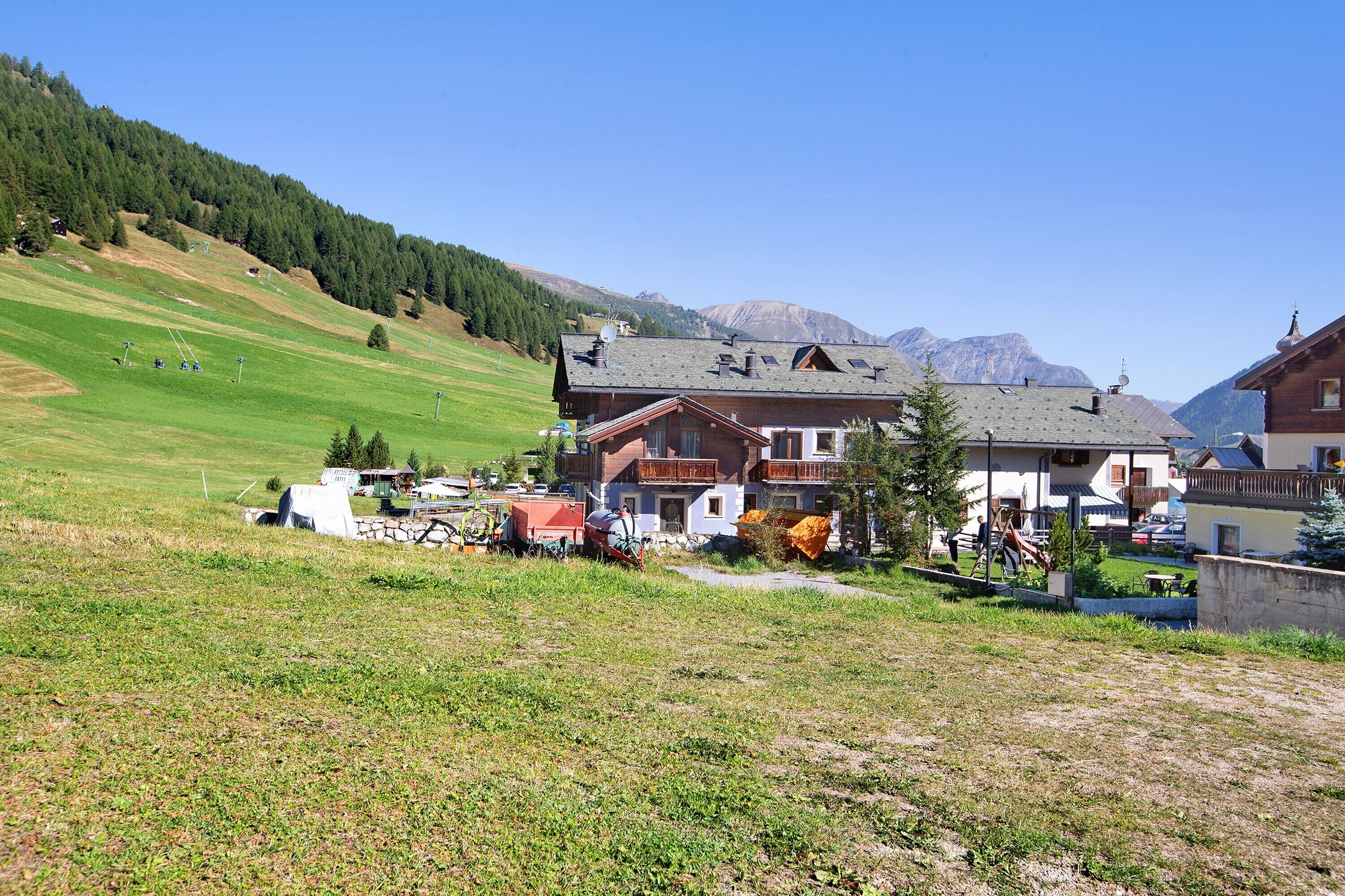 Un villaggio rurale con case tradizionali, un prato erboso e montagne sullo sfondo.