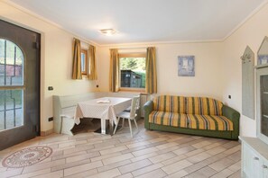 A room with a dining table, a sofa, a radiator, a window with curtains, and a door.