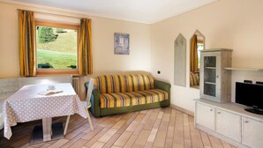 Een kamer met een tafel, bank, televisie en uitzicht op een groen landschap.