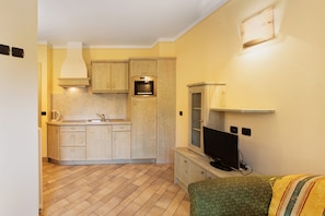 A compact kitchen with wooden cabinets, a built-in oven, and a television on a stand.